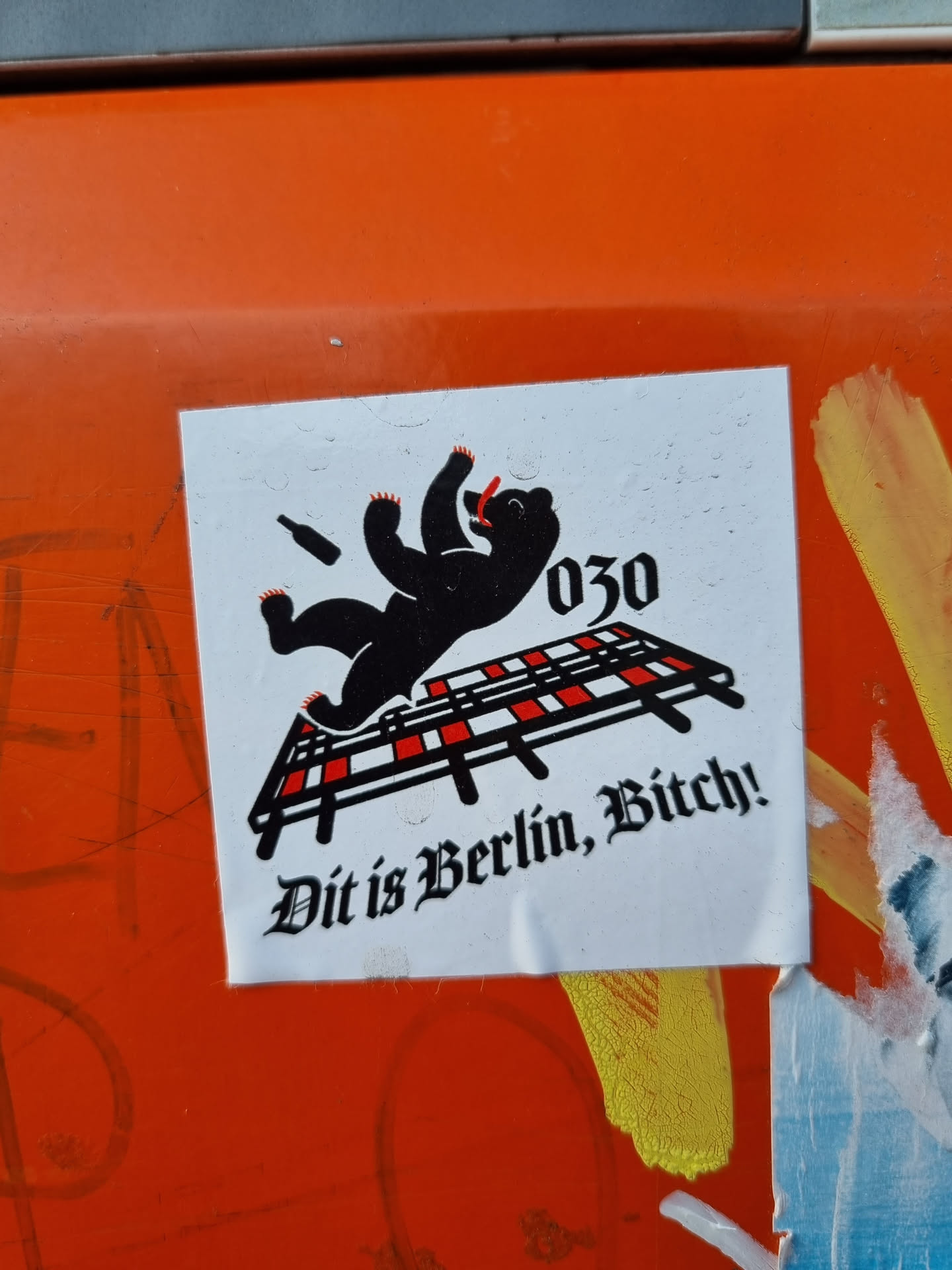 A sticker featuring a black bear lying on a red and white striped surface, possibly a cot or a bed frame. The bear seems to be intoxicated or passed out, with a bottle lying next to it. The text '030' and 'Dit is Berlin, Bitch!' are present on the sticker. The overall style is bold and slightly provocative.