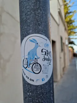 A sticker featuring a cartoon donkey riding a bicycle with panniers.  The sticker has a QR code linking to Steel Donkey's online presence, along with a Facebook logo.
