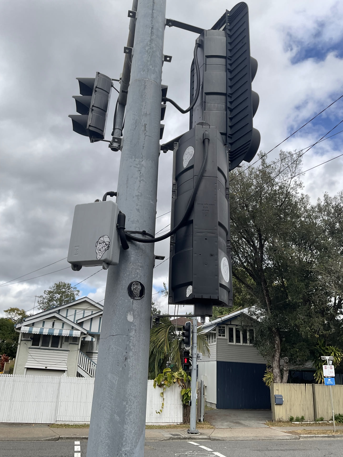 A small black oval sticker adhered to a metal traffic pole. It depicts a stylized, contour-line portrait of a smiling face with glasses or distinct facial creases in white lines. Beneath the portrait, the word 'FRANCO' is written in neat, white sans-serif uppercase letters.