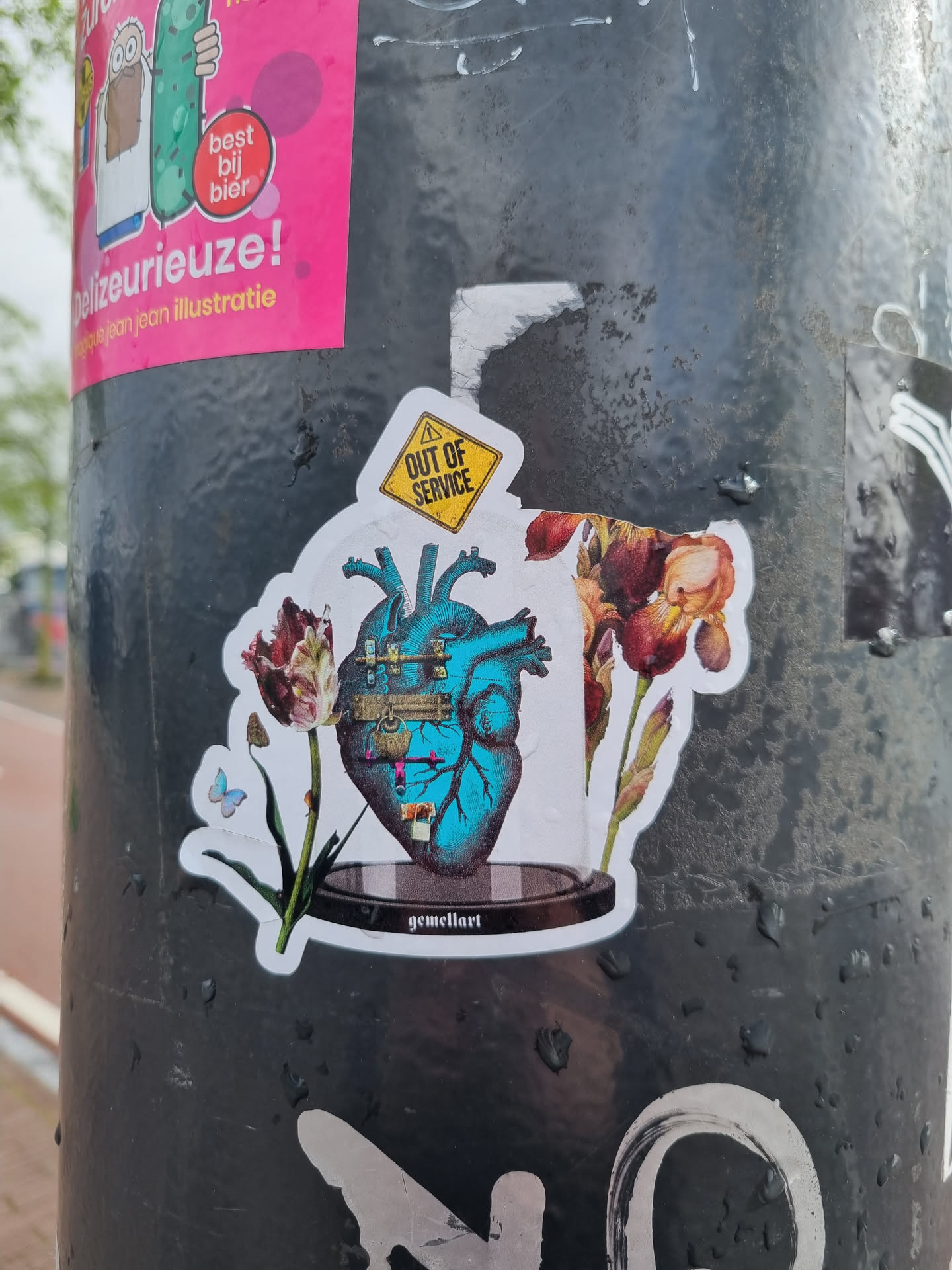 A sticker featuring a detailed illustration of a mechanical heart encased in glass, surrounded by flowers.  A small yellow diamond-shaped sign reading "OUT OF SERVICE" sits atop the heart. The artist's signature, "gemellart", is visible at the base.