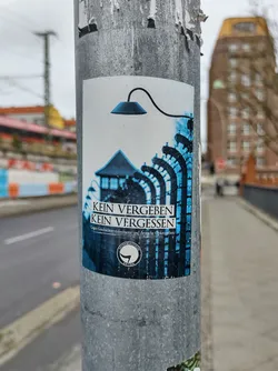 A sticker with a watchtower and barbed wire fence, symbolizing remembrance and against forgetting.  The text 'Kein vergeben Kein vergessen' (No forgiveness, No forgetting) is prominently displayed.