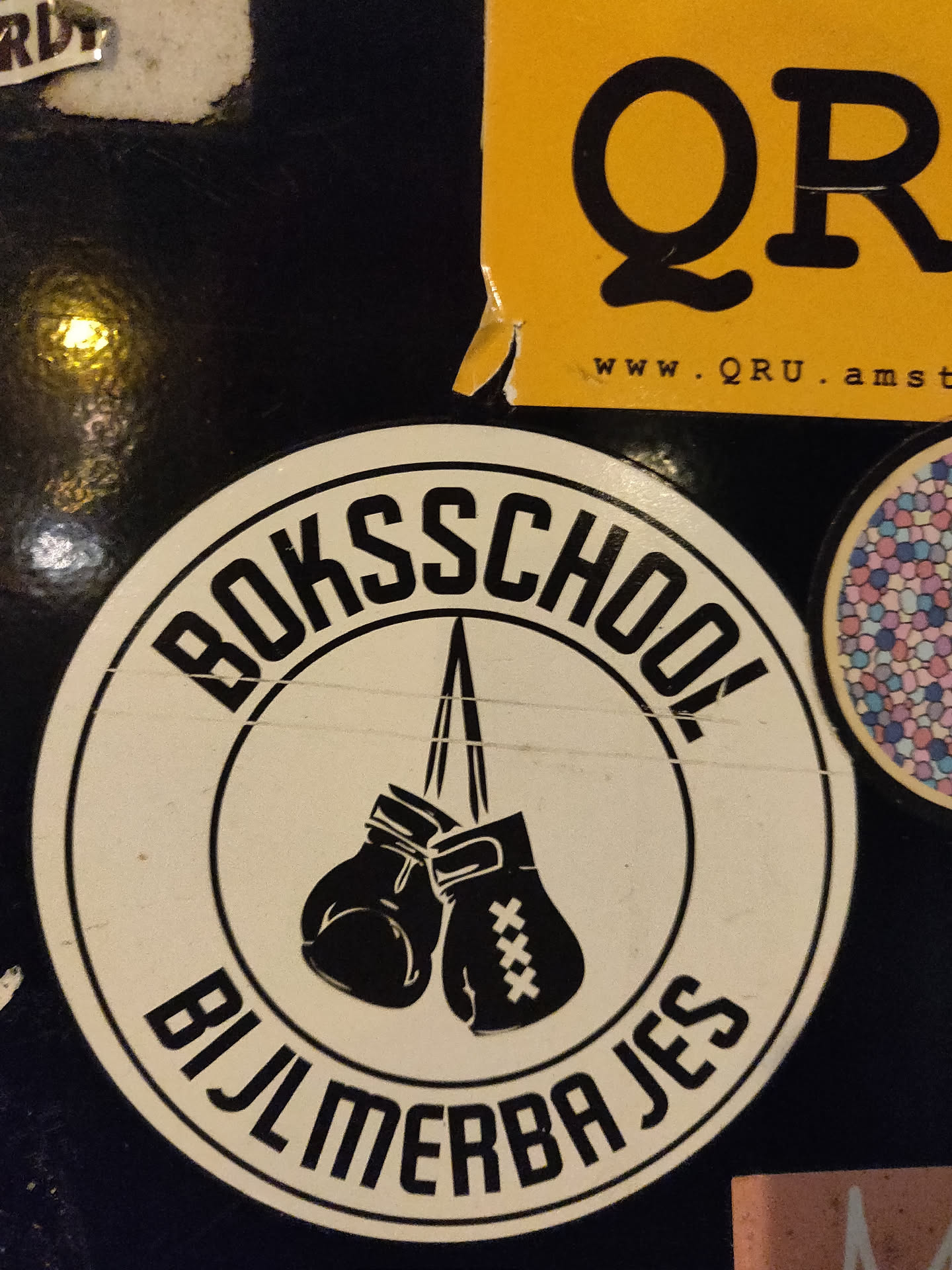 Round sticker with a black and white illustration of a pair of boxing gloves hanging from a rope. The text "Bokschool Bijlmerbajes" is written around the image of the gloves. 