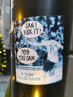 A sticker featuring a soccer player with a speech bubble saying "Can I kick it?" and a response bubble saying "Yes you can!" The text "A tribe called Bajen" is at the bottom. The player's jersey has the number 10 and the name KENNEDY.