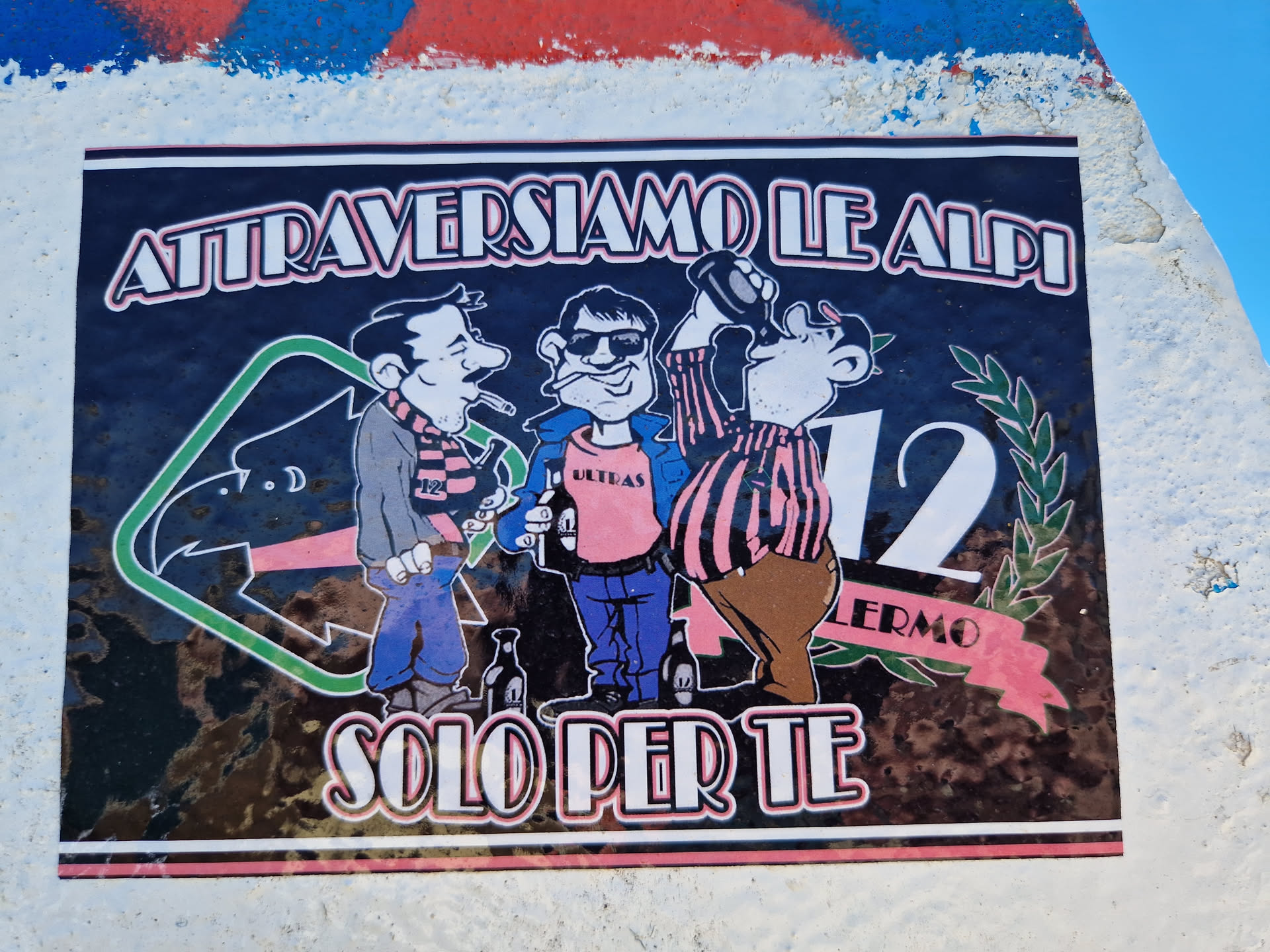 A sticker featuring a cartoon illustration of three men, possibly representing a mountaineering or hiking theme. The text 'Attraversiamo le Alpi' translates to 'Let's cross the Alps' in Italian.  'Solo per te' means 'Only for you'. The number 12 and the word 'LERMO' are also visible.