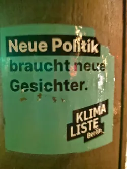 A teal and black sticker with the text "Neue Politik braucht neue Gesichter."  in white. At the bottom, it shows "KLIMA LISTE Berlin".