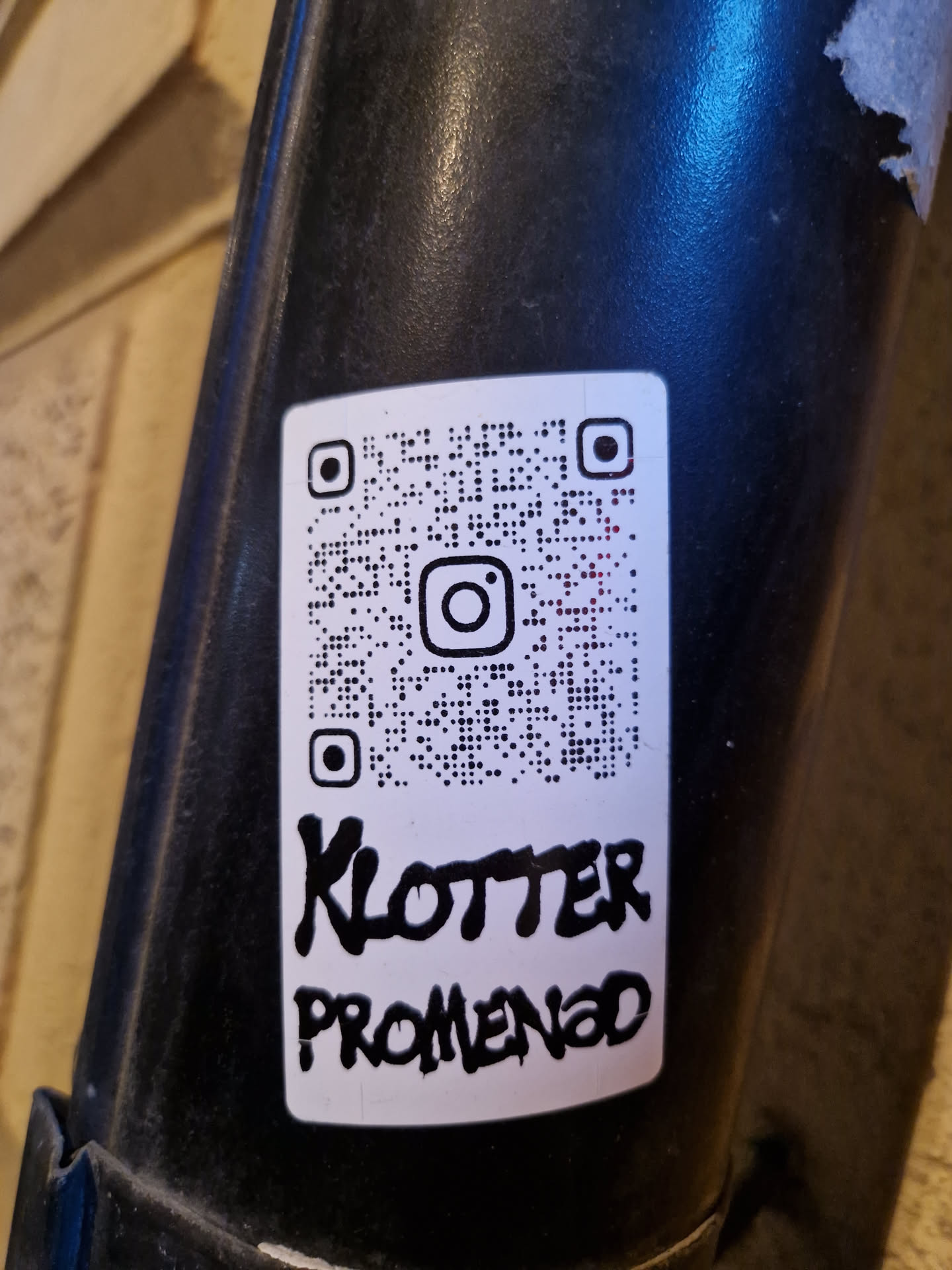 A white sticker with a QR code linking to Instagram and the text 'Klotter Promenad' written in black marker.