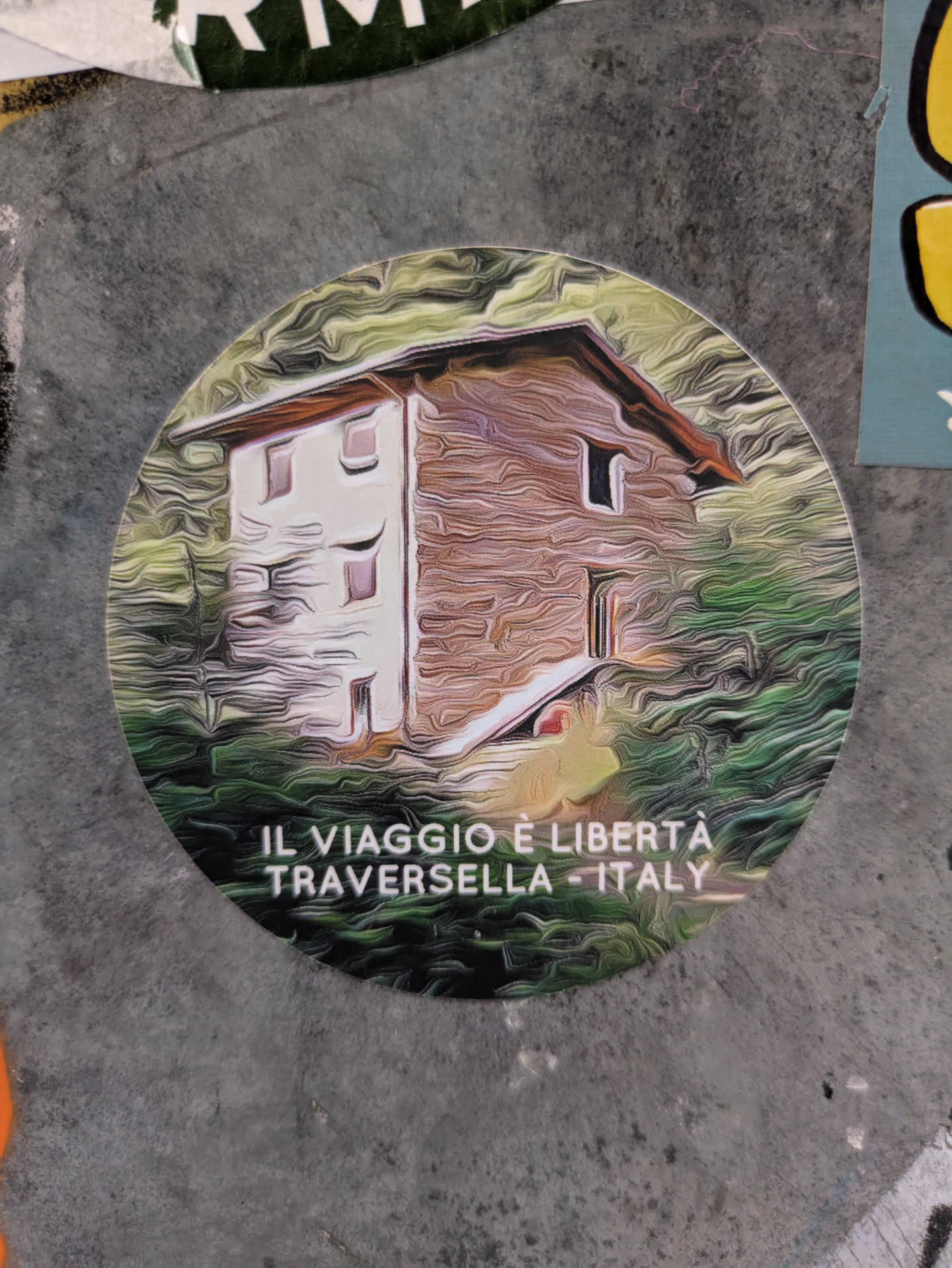 Round sticker featuring a stylized painting of a house in Traversella, Italy. The text at the bottom reads: "IL VIAGGIO È LIBERTÀ TRAVERSELLA - ITALY"