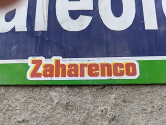 A sticker that says 'Zaharenco' in red with a yellow border on a white background. The sticker is placed on a green and blue sign.