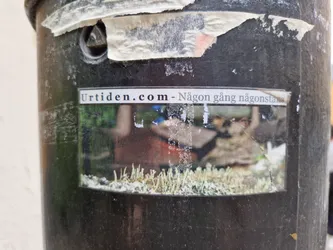 A sticker with a blurry image and text. The text on the top says "Urtiden.com - Någon gång någonstans". The image seems to depict a natural landscape.