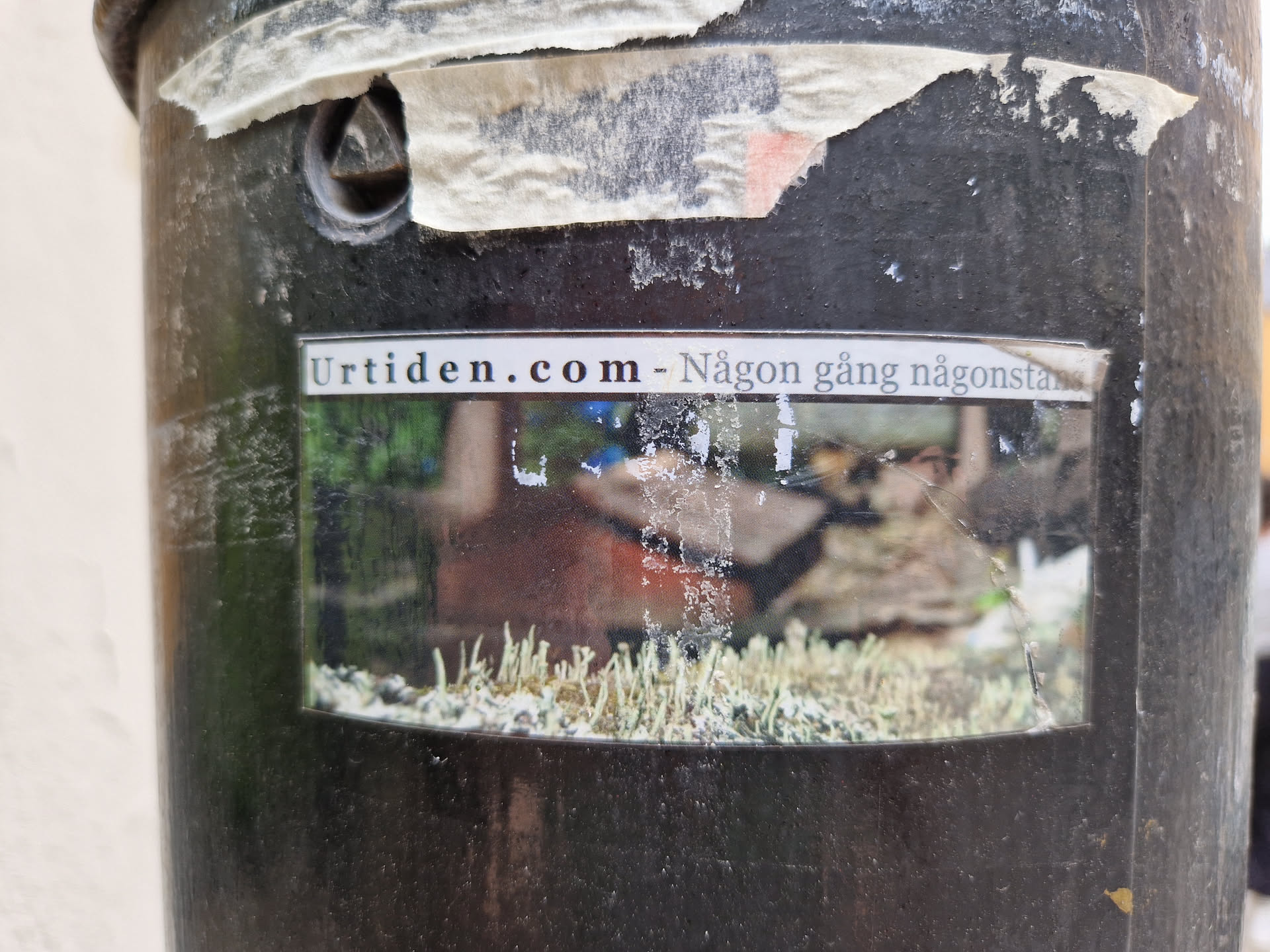 A sticker with a blurry image and text. The text on the top says "Urtiden.com - Någon gång någonstans". The image seems to depict a natural landscape.