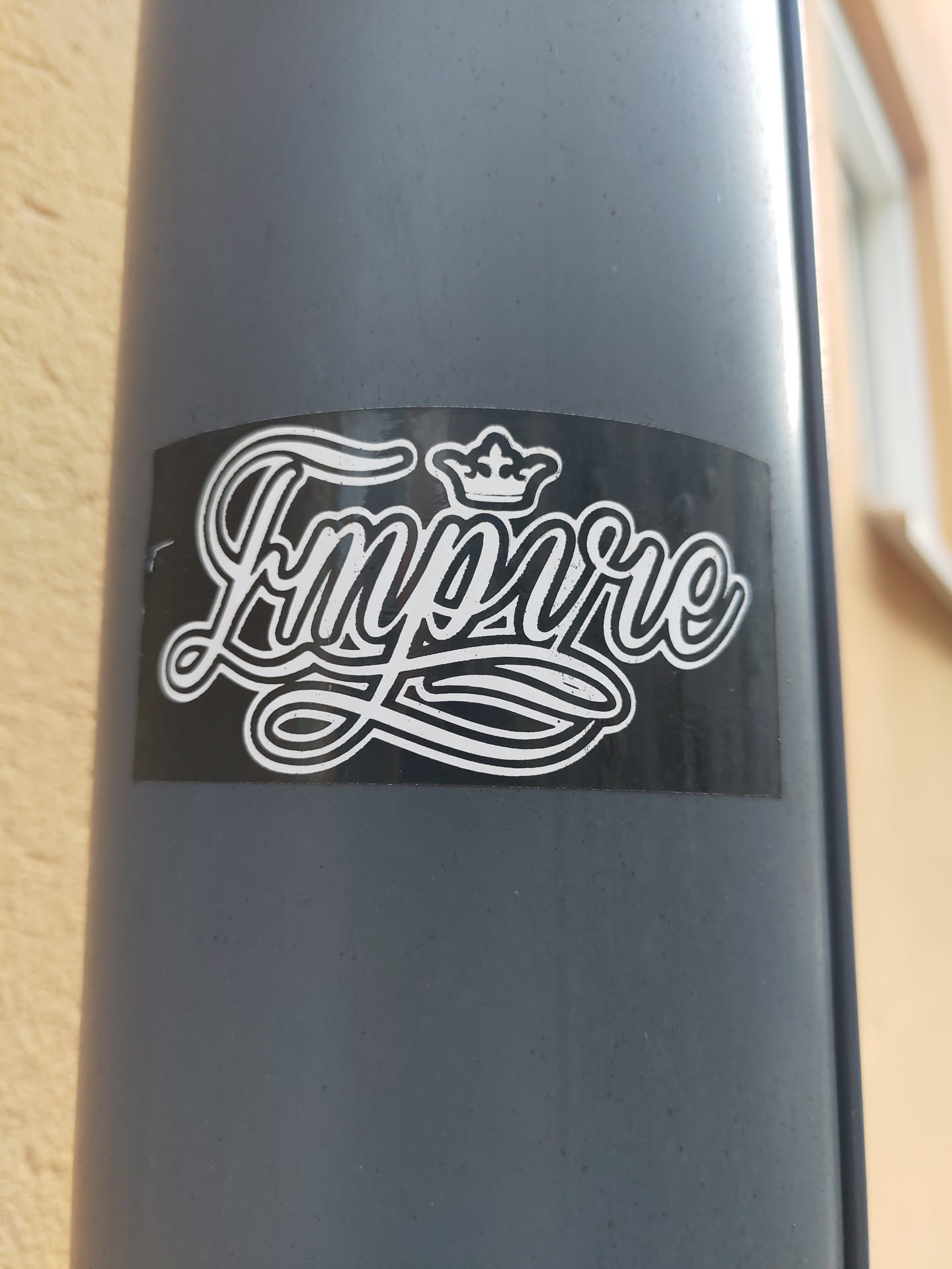 A black and white sticker with the word "Empire" stylized in a script font with a crown above it.  The sticker is affixed to a gray pole.