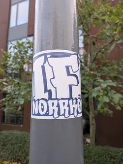 Street sticker A rectangular adhesive sticker wrapped around a cylindrical grey metal post. It features bold, graffiti-inspired lettering in white with a dark blue outline and shadow. The top half shows large stylized letters reading 'IF', while the bottom line displays 'NORRKÖ' with small decorative dots forming an umlaut above the 'O', representing the Swedish football club IFK Norrköping.