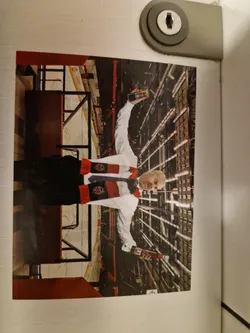A sticker depicting a man in a red and black scarf and white shirt holding two bottles of HP Sauce. He is standing in what appears to be a hockey stadium. The image is vibrant, the man appears joyful, and the background shows the interior structure of a sports facility.