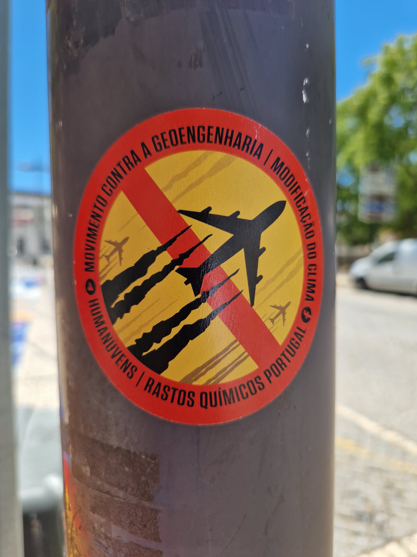 Sticker expressing opposition to geoengineering and climate modification. It depicts a plane with a red cross over it, symbolizing a rejection of these practices. The text includes the Portuguese words for "Movement Against Geoengineering", "Modification of the Climate", and "Chemtrails".