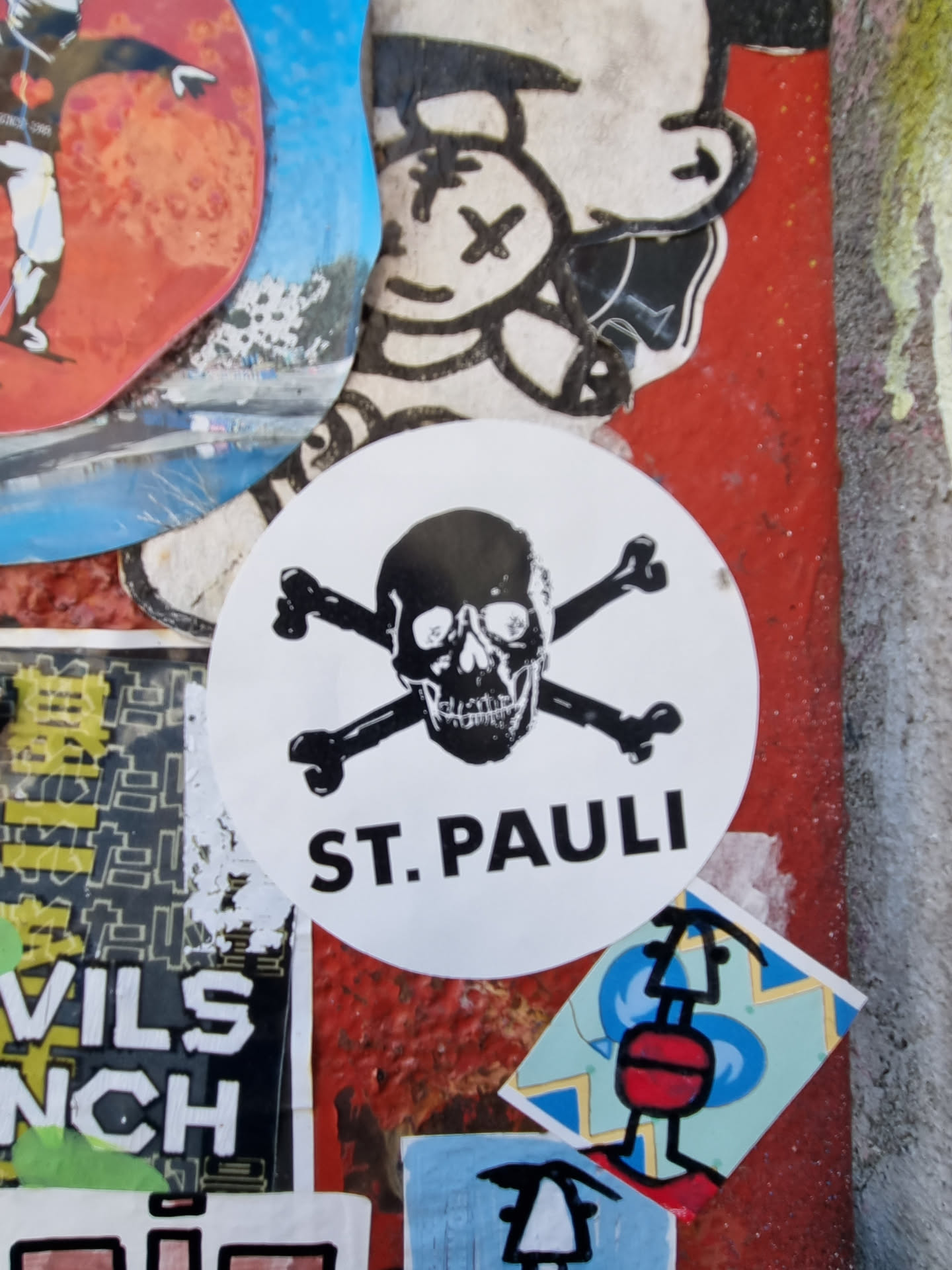 A round sticker with a skull and crossbones design and the text "ST. PAULI" underneath. The sticker is white with black ink. 