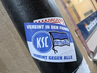 A sticker showing the logo of Hertha BSC and KSC, with the text "Vereint in den Farben" (United in the colors) and "Vereint gegen alle" (United against all).