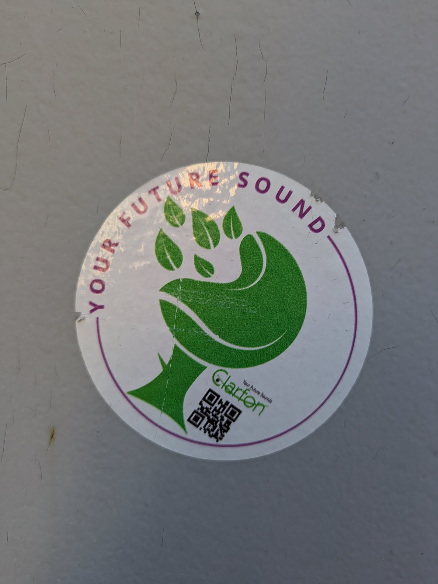 A round, white sticker with a stylized green hand/paw design with leaf-like fingers. The sticker reads "YOUR FUTURE SOUND" around the top circumference. Below the hand graphic, the name "Clarføn" is printed in small black text above a QR code.