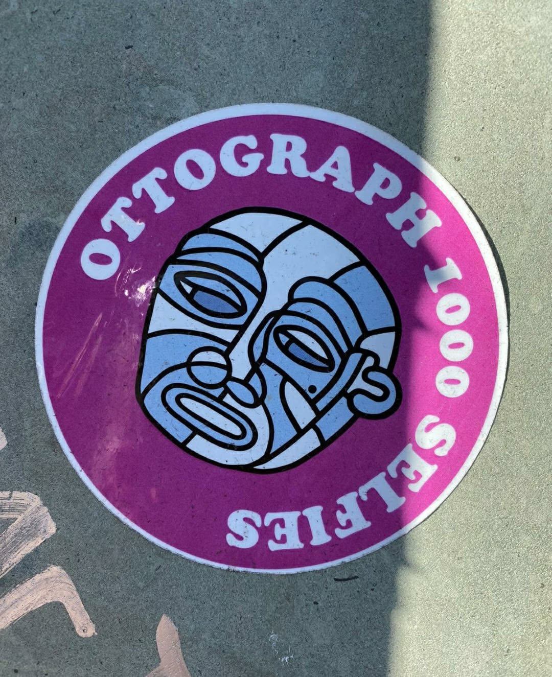 Round sticker with a purple background featuring a stylized illustration of two faces and the text "Ottograph 1000 Selfies".