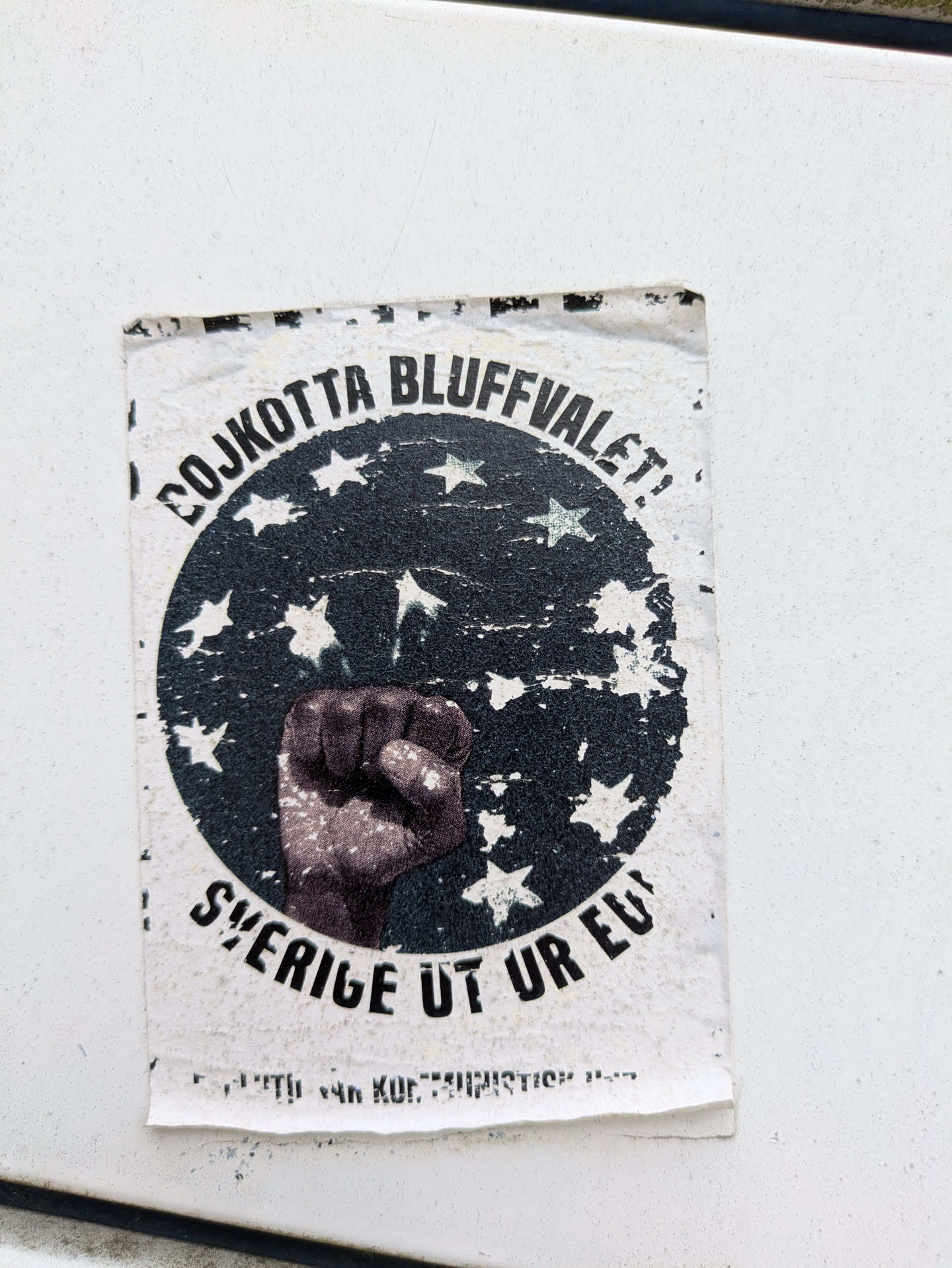 A slightly weathered sticker with a black and white design. The sticker features a circular design with stars and a raised fist in the center. The text reads "BOJKOTTA BLUFFVALET!" at the top and "SVERIGE UT UR EU!" at the bottom.