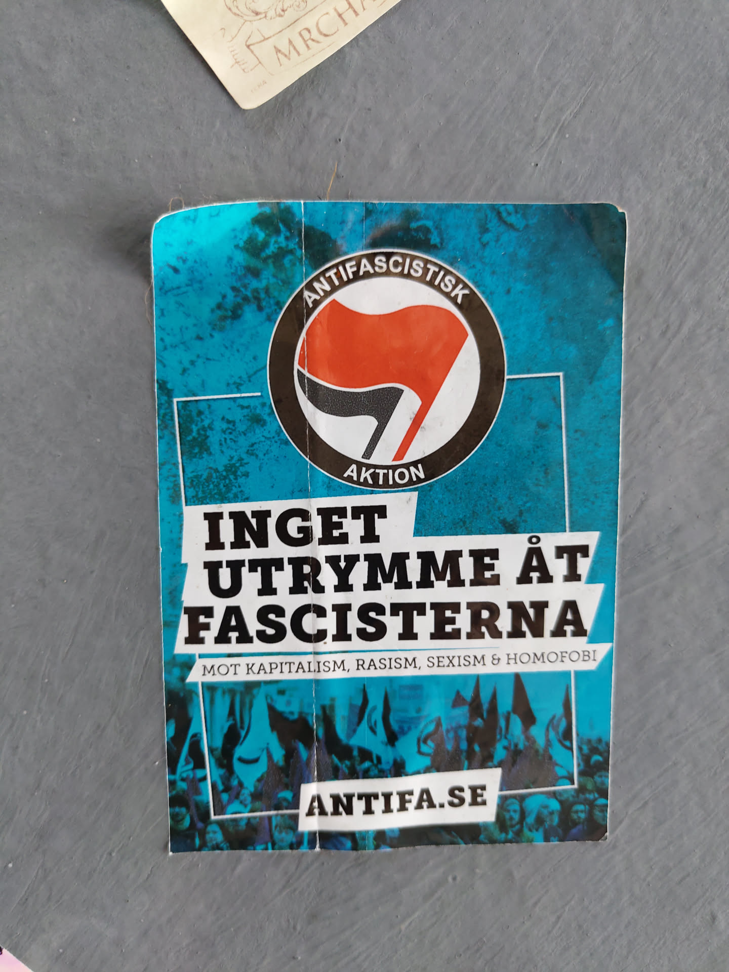 A sticker with a black and red flag symbol, the text "INGET UTRYMME ÅT FASCISTERNA" (No room for fascists) and the website antifa.se. The sticker advocates against capitalism, racism, sexism, and homophobia.