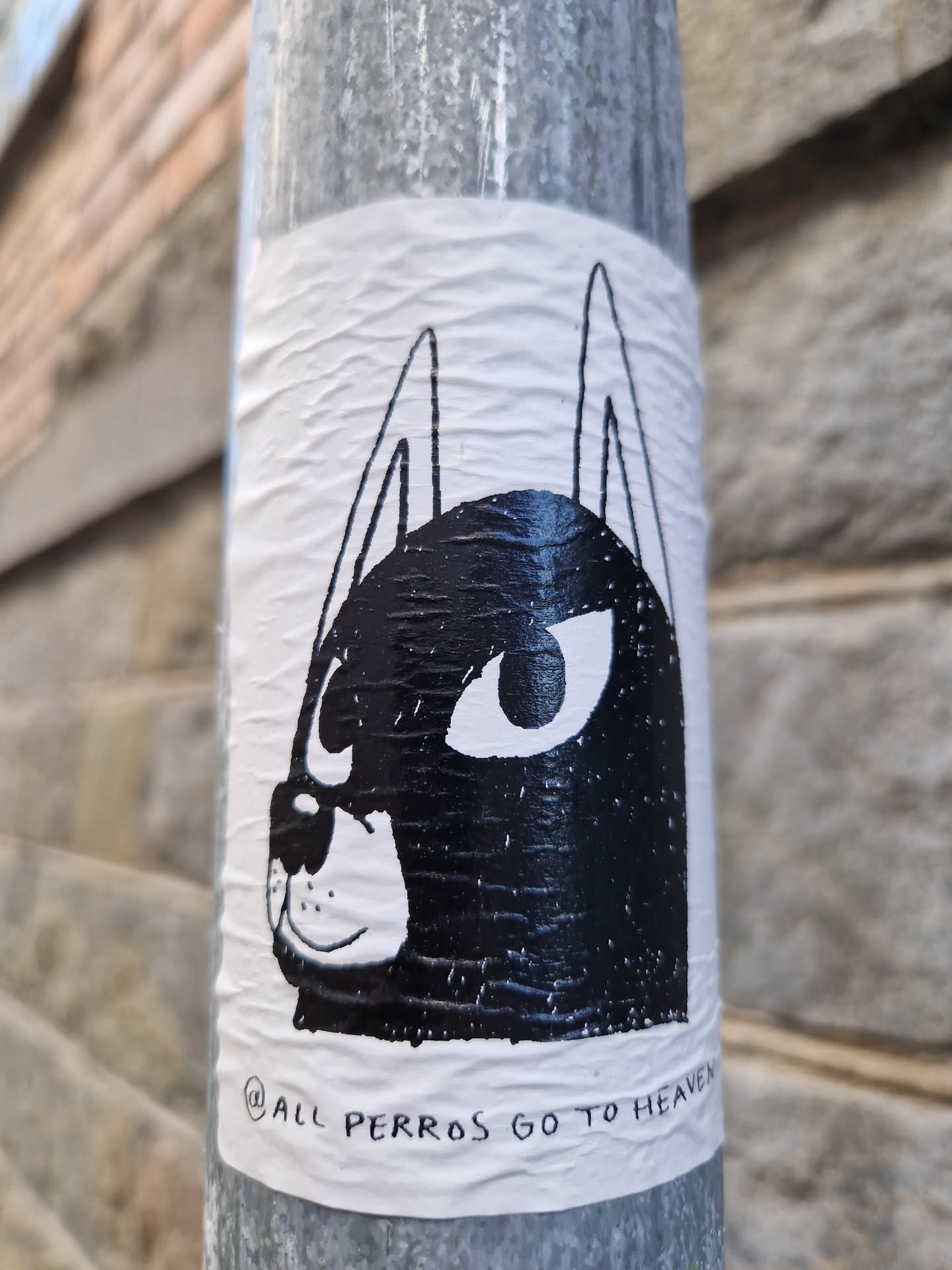 A black and white sticker of a dog's face with big eyes. The text at the bottom says "All perros go to heaven".