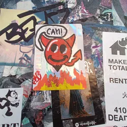 Holographic sticker of a smiling devil character with flames at the bottom. The devil is red and has a speech bubble saying "Can!"