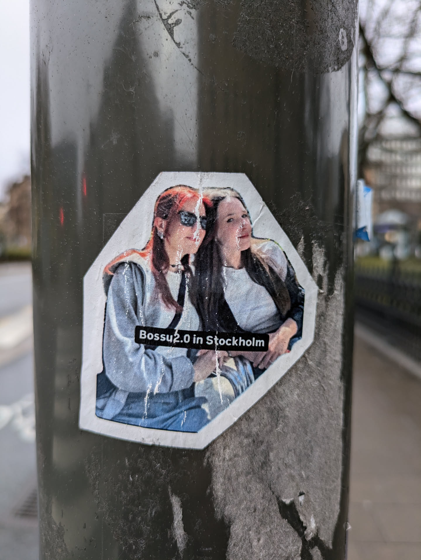 A sticker featuring a photo of two women, likely in Stockholm, Sweden.  The sticker has a slightly damaged appearance.