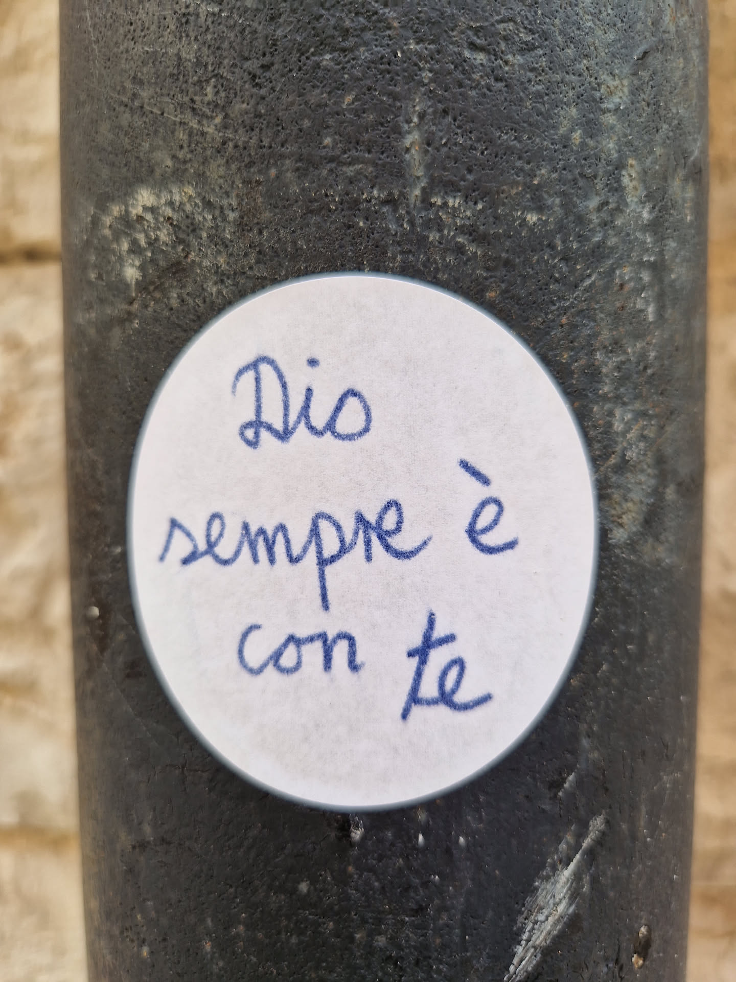 A round white sticker with a handwritten message in blue ink. The message reads: "Dio sempre è con te." which translates from Italian to: "God is always with you."