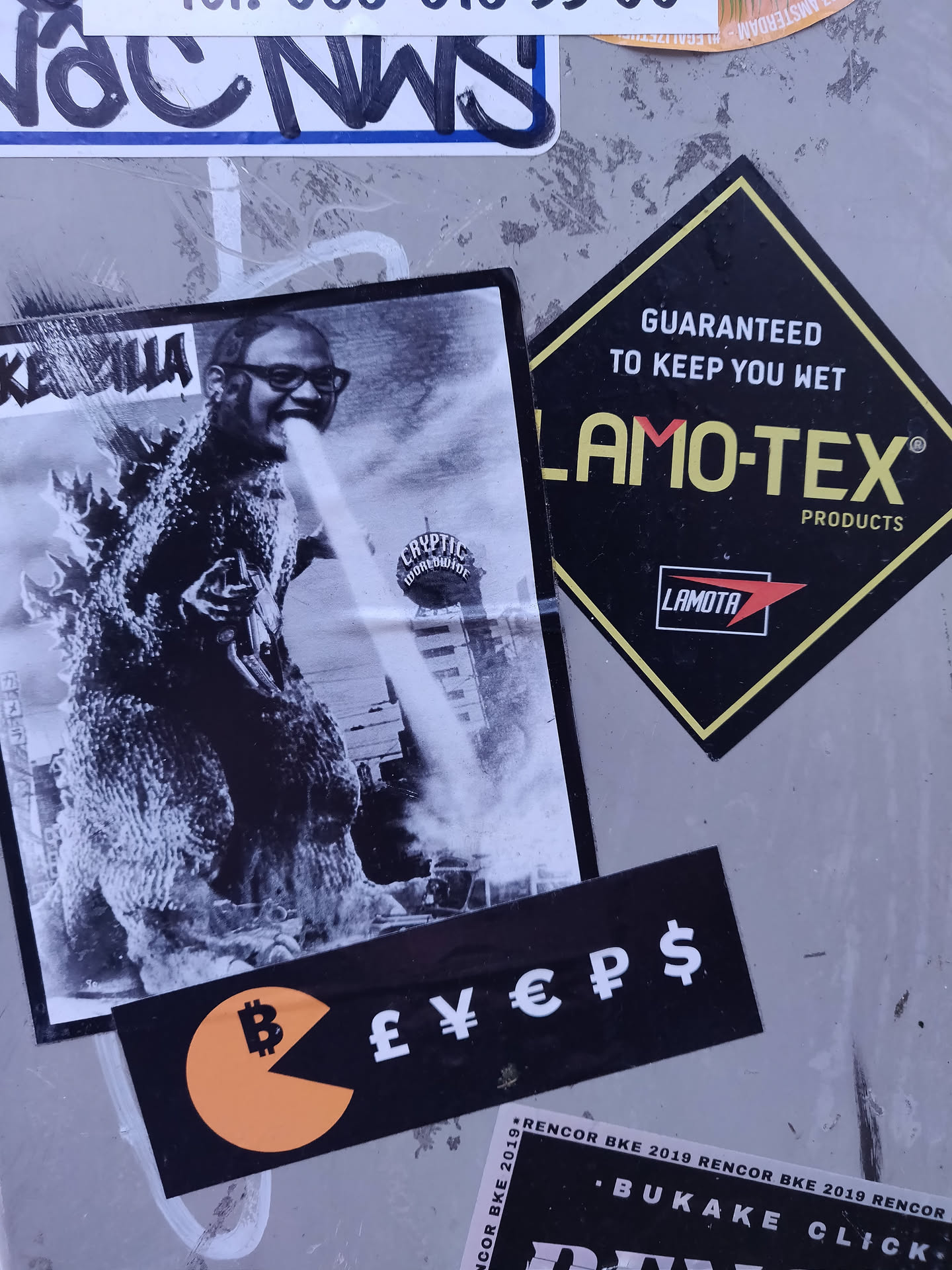 A sticker featuring a black and white image of Godzilla seemingly breathing fire onto a person wearing glasses.  Below is a smaller sticker with a Pac-Man-like shape, containing a Bitcoin symbol and various currency symbols.